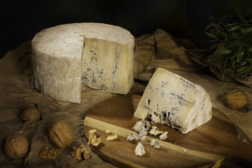 Se muestra un queso azul con una cuña cortada. Se aprecian las vetas azules en el interior del queso. Junto al queso hay algunas nueces.