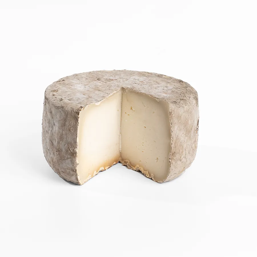 Se muestra un queso entero de corteza gris e interior blanco compacto, al que se le ha cortado una cuña.