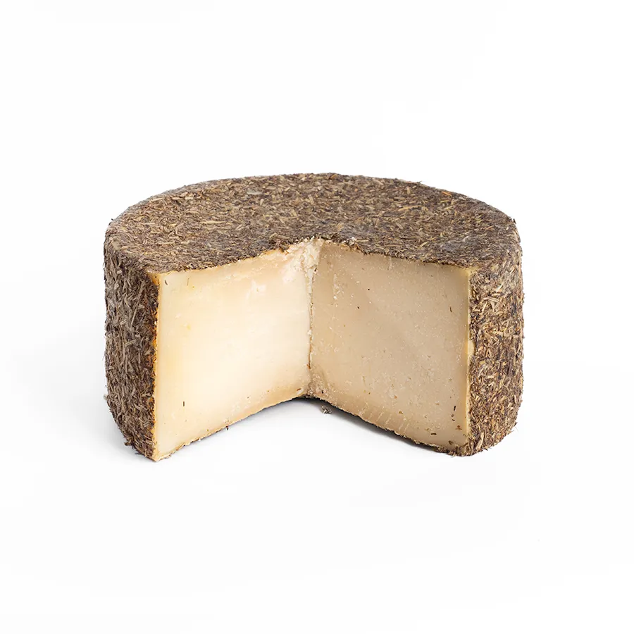 Se muestra un queso con corteza cubierta de tomillo y con una cuña cortada, de modo que se aprecia el interior del queso con una textura compacta.