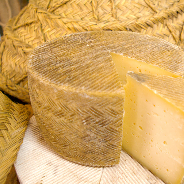 Se muestra un queso de corteza rugosa y amarillenta con una cuña cortada.