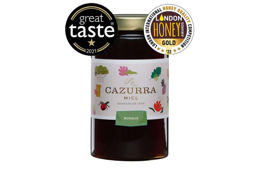Se muestra un bote de miel con dos de los premios recibidos: la medalla del Great Taste y el ORO en los London Honey Awards