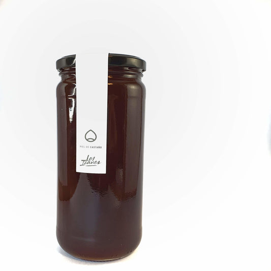 Se muestra un tarro de miel de castaño muy oscura sobre un fondo blanco.