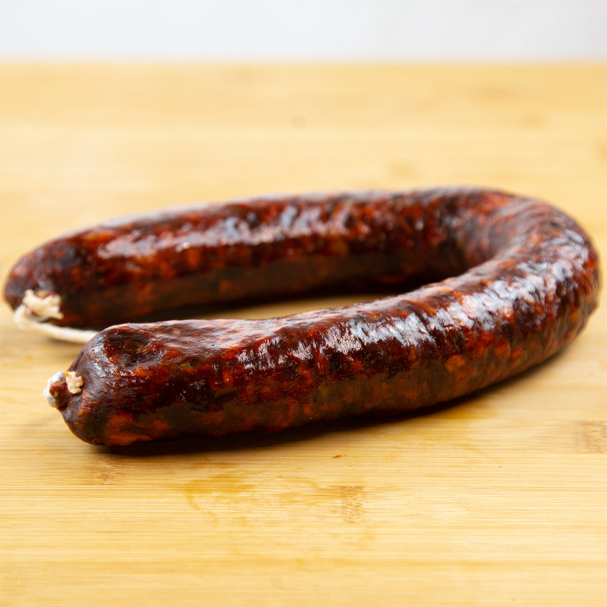 Muestra un chorizo de jabalí en herradura. Está sobre una tabla de madera de color marrón claro.