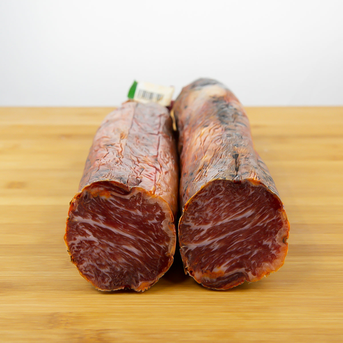 Lomo ibérico cortado en el que se aprecia el infiltrado de grasa en su carne. Hay dos mitades sobre una tabla marrón claro.