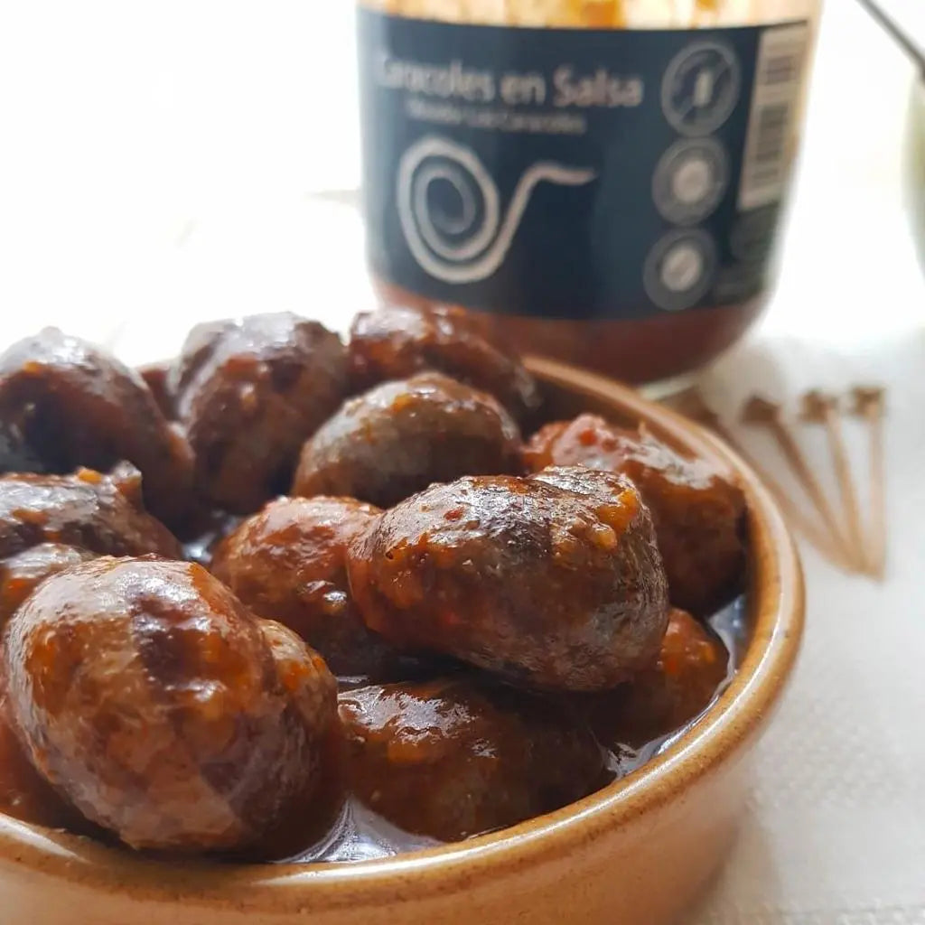 Se muestra un plato de caracoles en salsa.