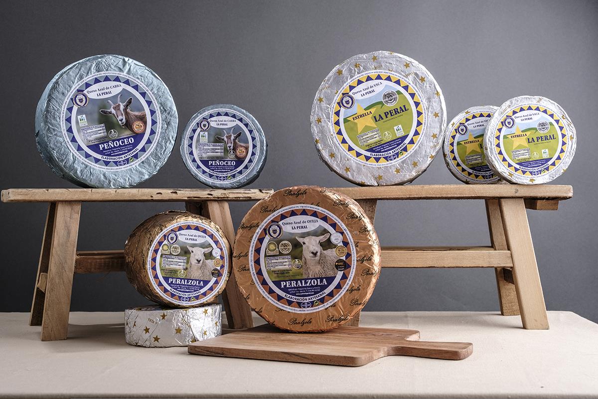 Se muestran varios quesos de distintos tamaño cubiertos por distintas envolturas de papel. Son los quesos Estrella, Peñoceo y Peralzola.