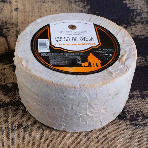 Se muestra un queso entero cubierto de manteca blanca. En la base superior del queso aparece la etiqueta del productor con la información del queso.