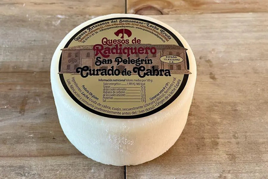 Se muestra un queso entero con su etiqueta sobre una superficie de madera.