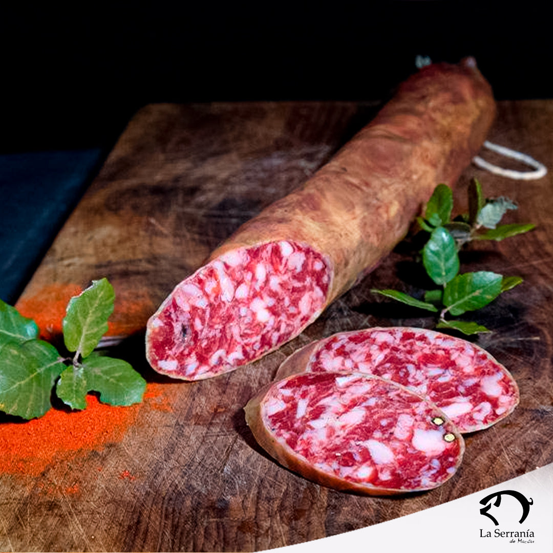 Se muestra un salchichón ibérico cular con dos rodajas cortadas sobre una tabla de madera. Se aprecia la grasa del embutido y tiene muy buen aspecto.