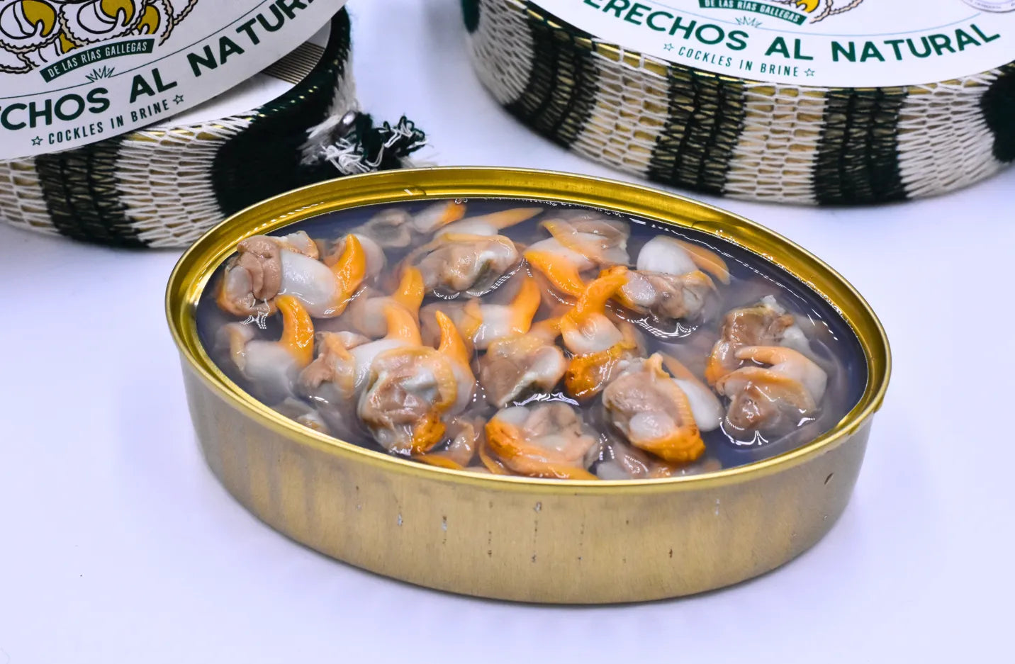 Se muestra una lata de berberechos abierta. En la parte superior de la imagen se ven parcialmente dos latas más.