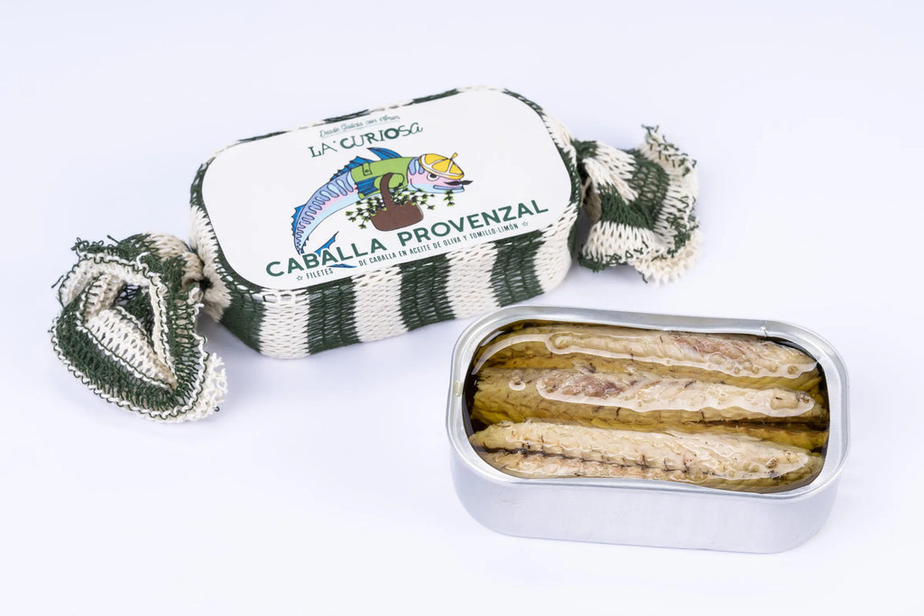 Se muestran dos latas de caballa en aceite, una de las latas está envuelta en una tela y otra no tiene tapa y se ven las caballas.