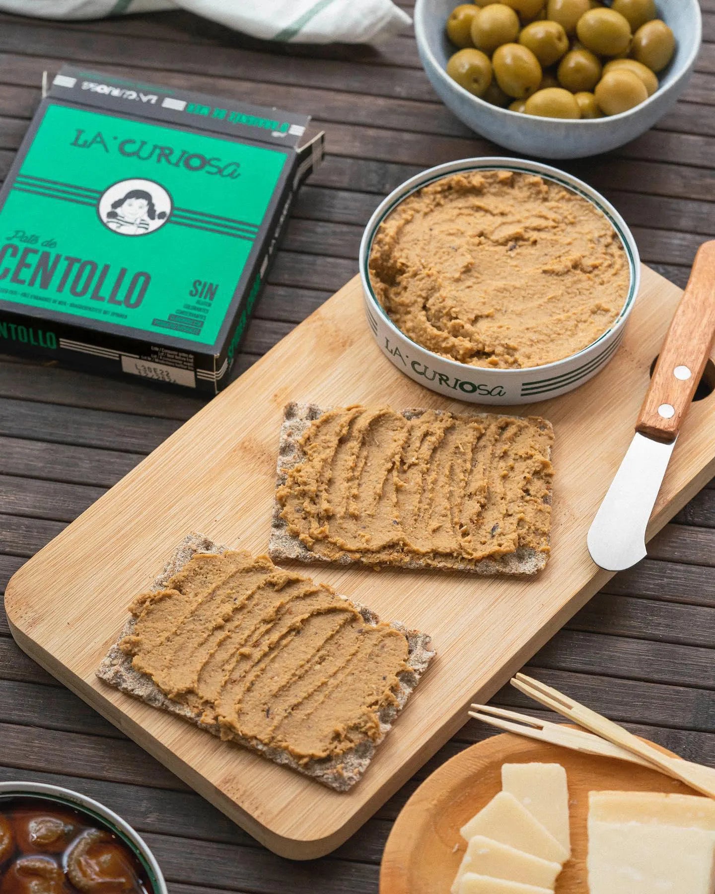 Se muestra una lata de paté con dos canapés untados con ese paté. Arriba se muestra la caja en la que viene el paté.