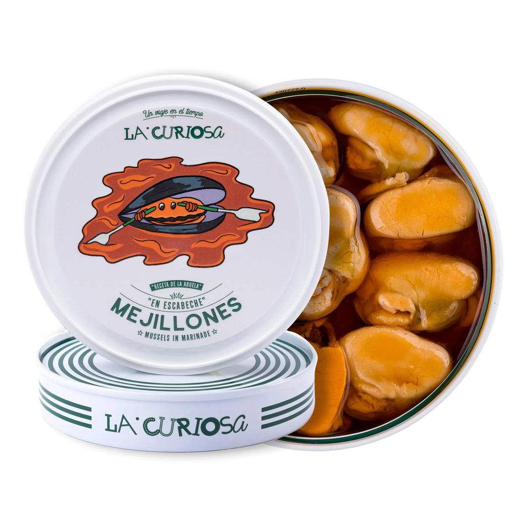 Se muestran dos latas de mejillones, una de ellas de canto sobre la otra, de modo que se aprecia la tapa de la lata. Una tercera lata está abierta y con mejillones atrás de la foto.