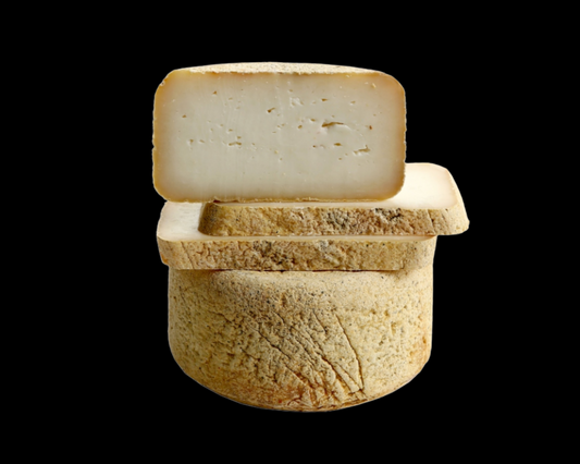 Se muestra un queso madurado partido a la mitad puesto una parte sobre la otra. Se puede apreciar la textura del interior y la corteza rugosa. El fondo de la imagen es negro.