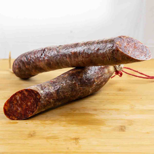 Se muestra un chorizo cular cortado en dos mitades sobre una tabla marrón claro. 