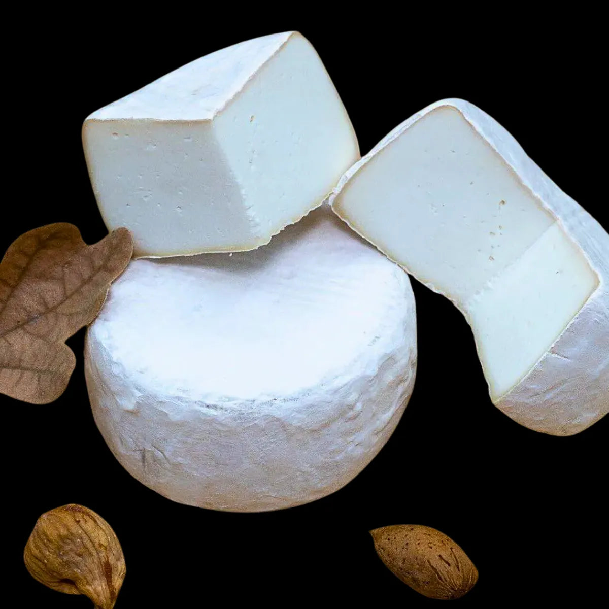 Se muestra un queso entero y uno partido. Ambos quesos están sobre un fondo negro y tiene una corteza muy blanca.