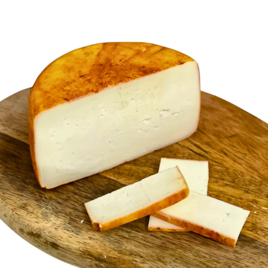 Queso semicurado sobre cortado a la mitad y algunos cachos sobre una tabla de madera. 