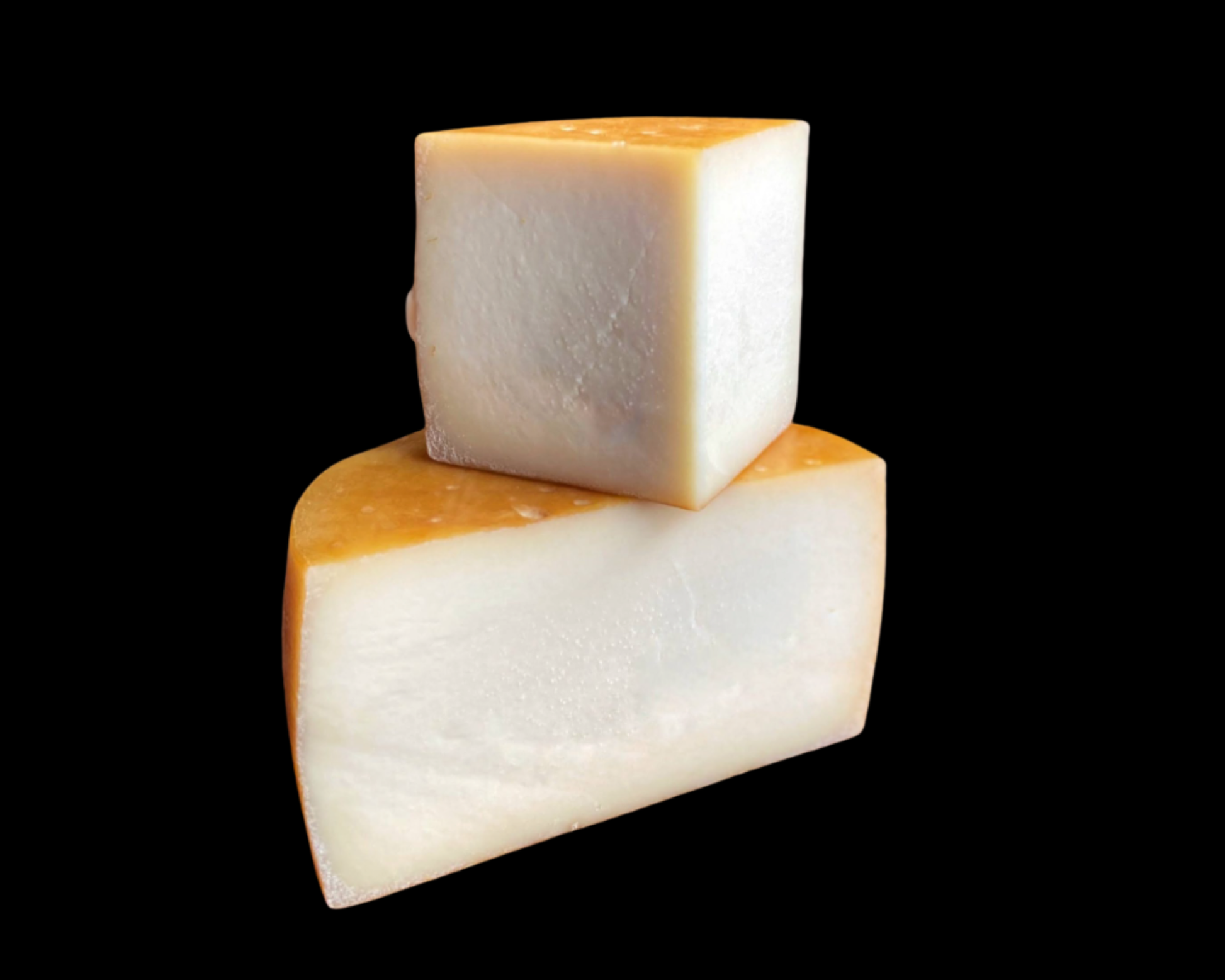 Se muesta medio queso dop idiazabal ahumado cortado por la mitad, con una cuña sobre la mitad cortada. Se aprecia su textura sobre el fondo negro de la imagen. La corteza del queso es anaranjada, propia del queso ahumado.