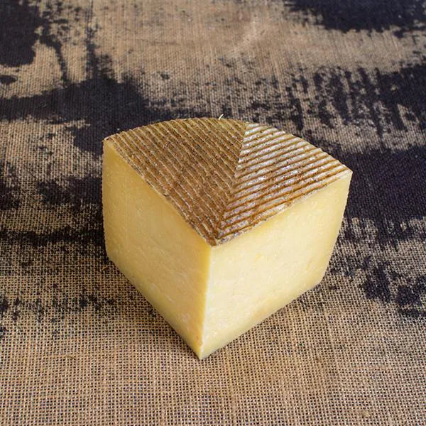 Se muestra una cuña de queso de color amarillenta y textura firme.