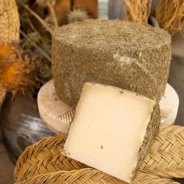 Se muestra un queso recubierto de romero y una cuña cortada.