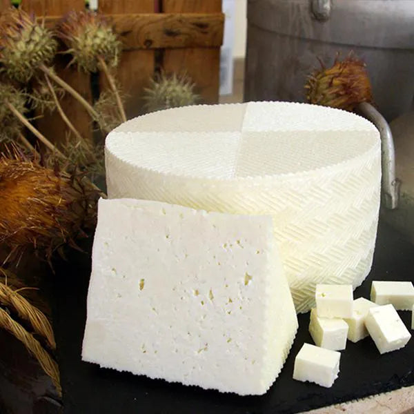 Se muestra un queso entero, una cuña y varios cachos pequeños de queso tierno. Todas las porciones son de color blanco.