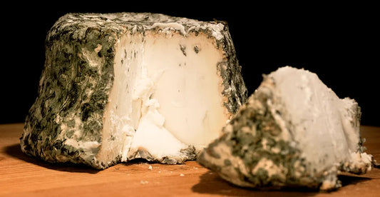 Queso entero con una cuña cortada. Se aprecia el interior blanco del queso y el exterior recubierto de moho.