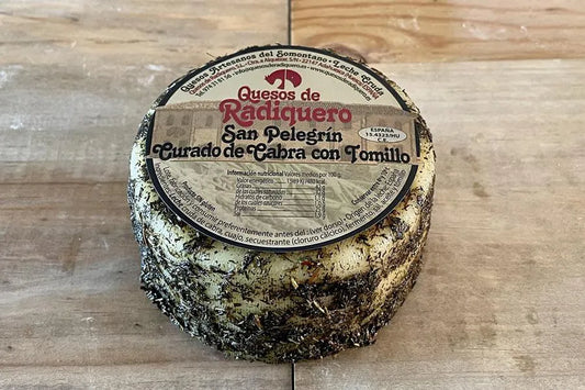 Se muestra un queso con su corteza bañada en tomillo sobre una superficie de madera.