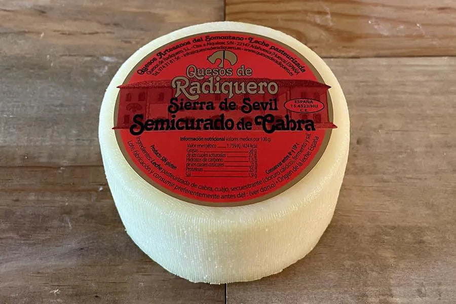 Queso de corteza muy blanco con una etiqueta roja en su base superior. El queso está sobre una superficie de madera.