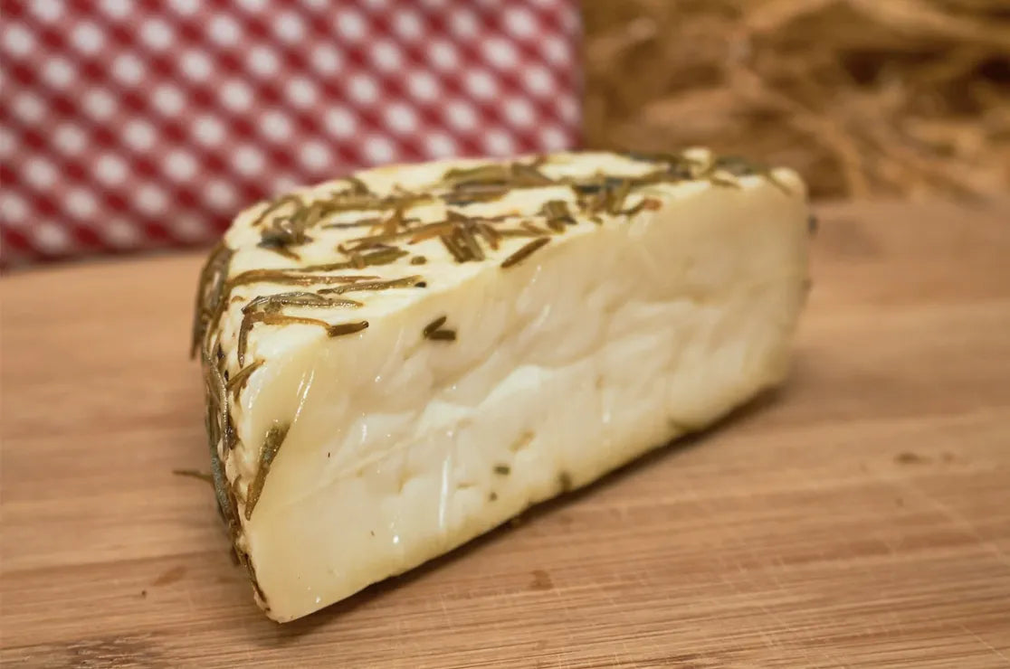 Cuña de queso en la que se aprecia el romero sobre una tabla de madera.