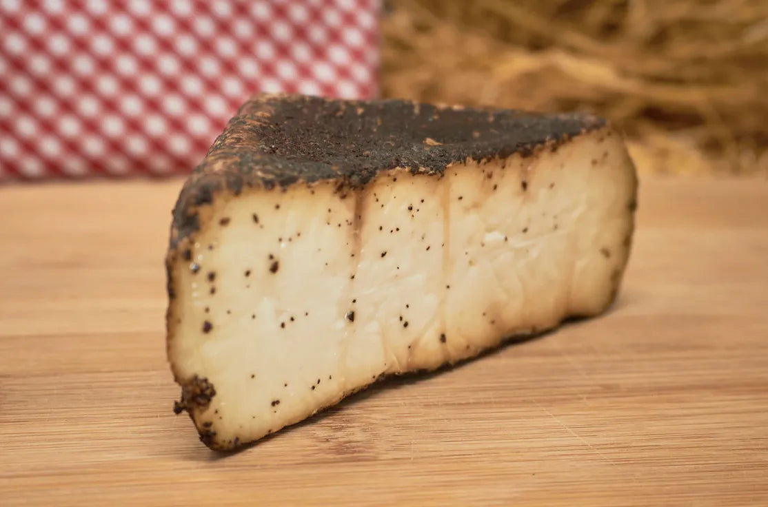 Cuña de queso en la que se muestra la cobertura de café. El queso está sobre una tabla de madera.