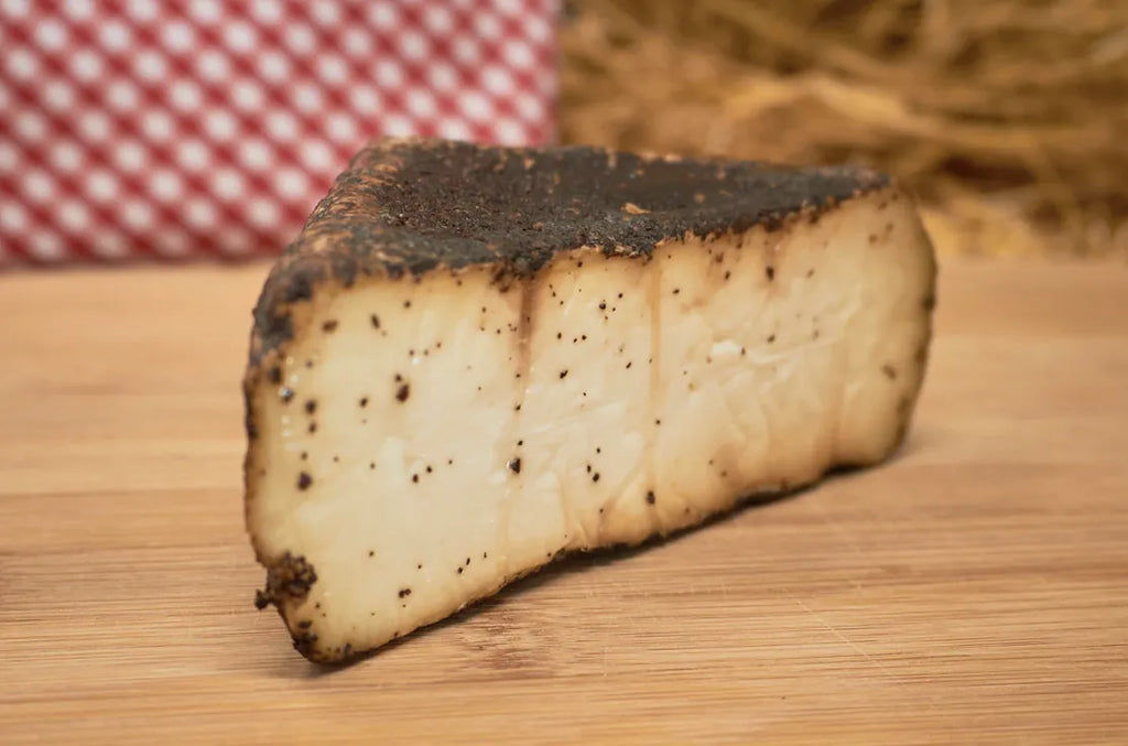 Cuña de queso en la que se muestra la cobertura de café. El queso está sobre una tabla de madera.
