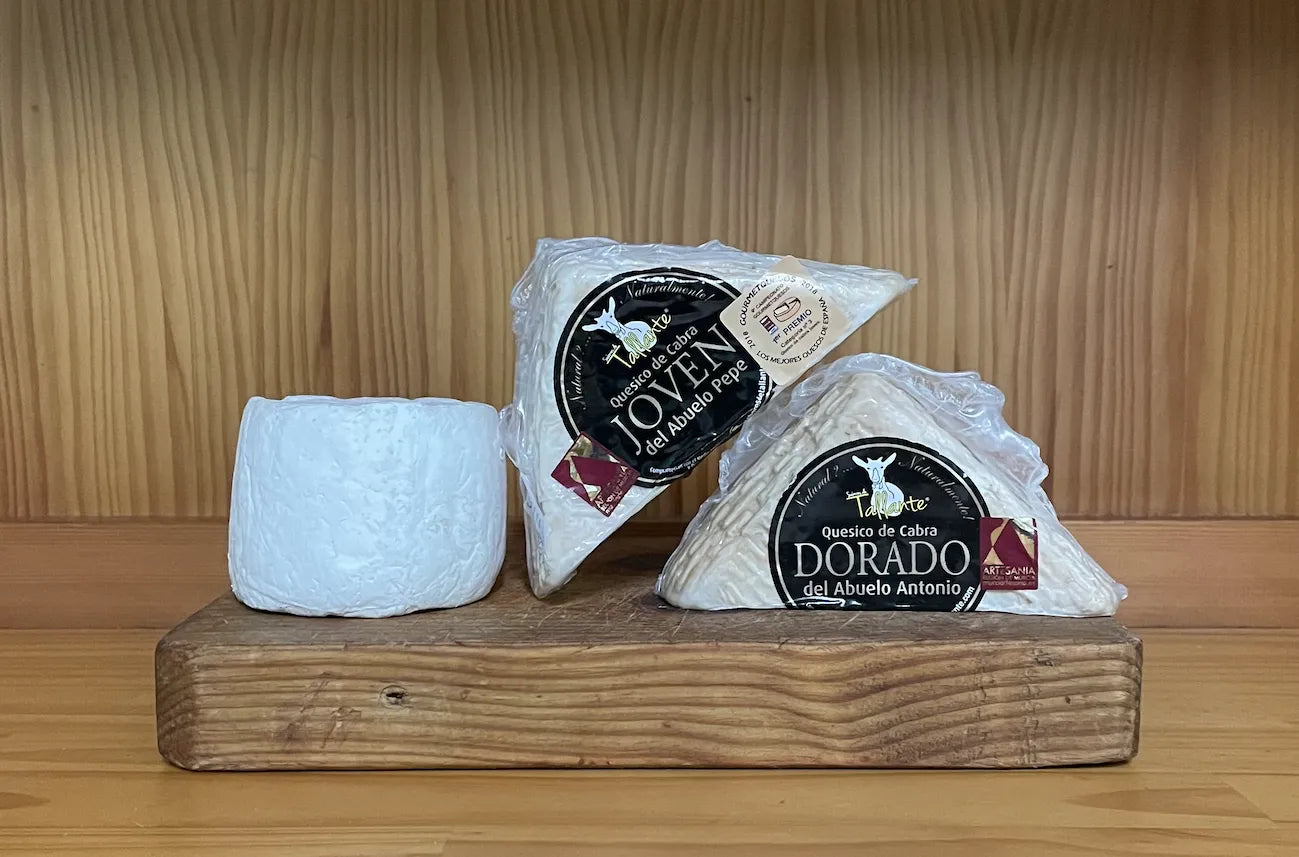 Se muestran 3 quesos, dos en forma de cuña y uno redondo. Los tres quesos están sobre una tabla de madera.