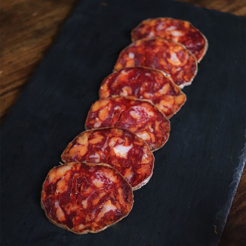Se muestran varias rodajas del chorizo cortado sobre una tabla de pizarra negra.