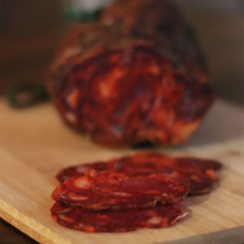 Se muestra un chorizo al fondo y varias rodajas en primer plano, y todo ello sobre una tabla de madera.